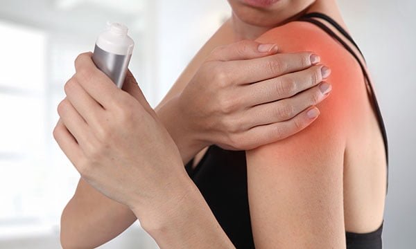 Woman suffering from shoulder back pain applying pain relief cream . Sports exercising injury.